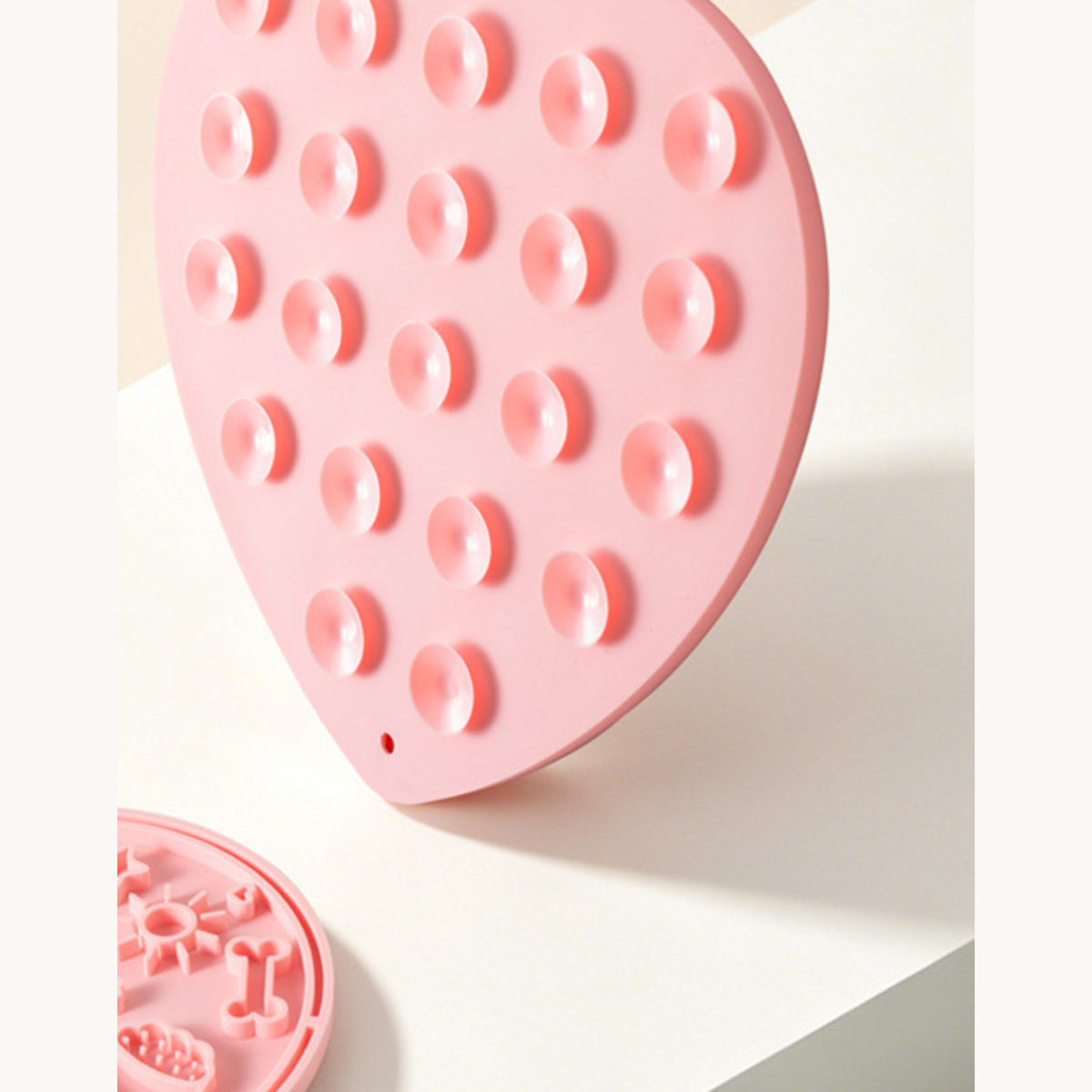 Pink heart-shaped lick mat tilted to show the suction cups on the back