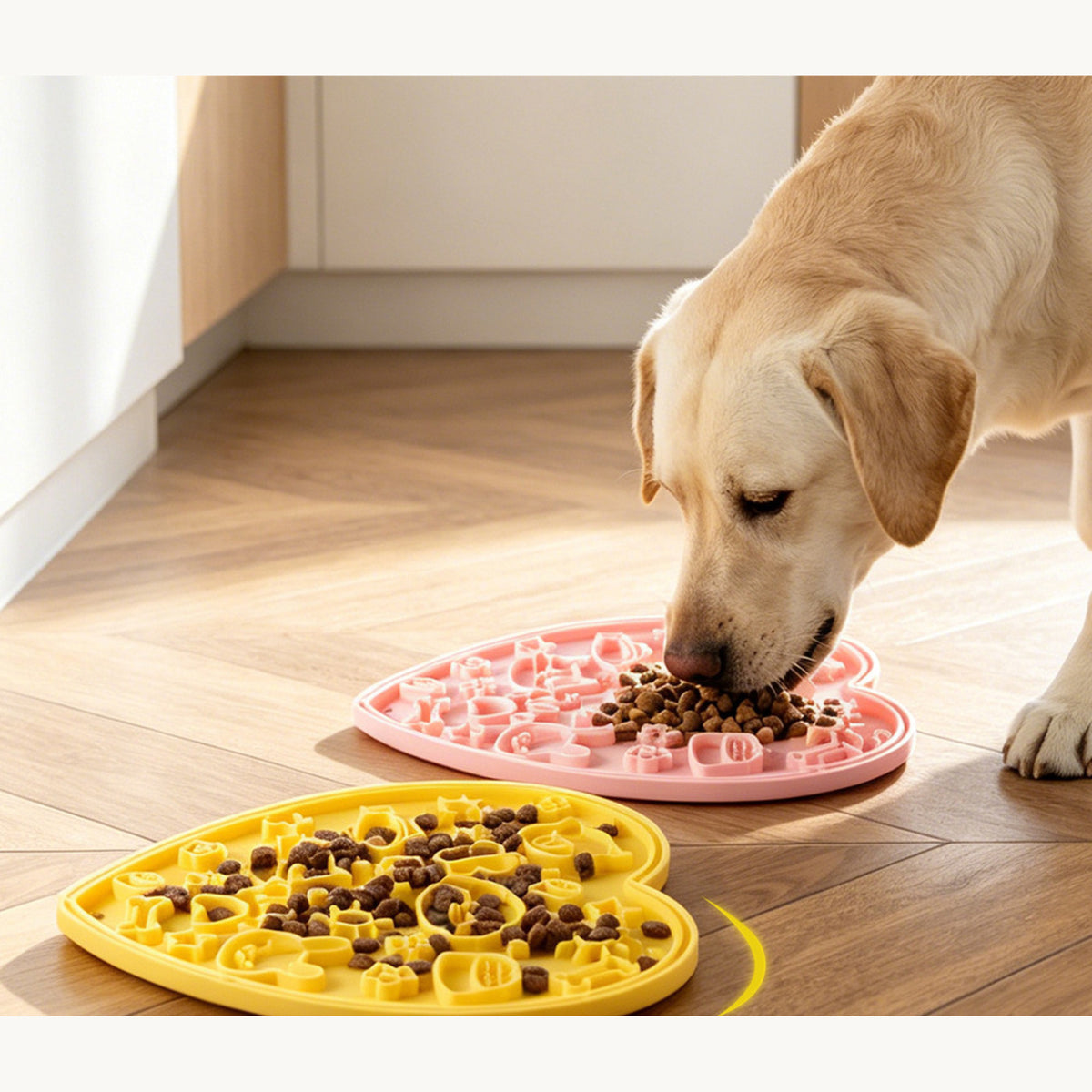 Labrador licking food from the yellow heart-shaped lick mat on a wooden floor, a pink one beside it